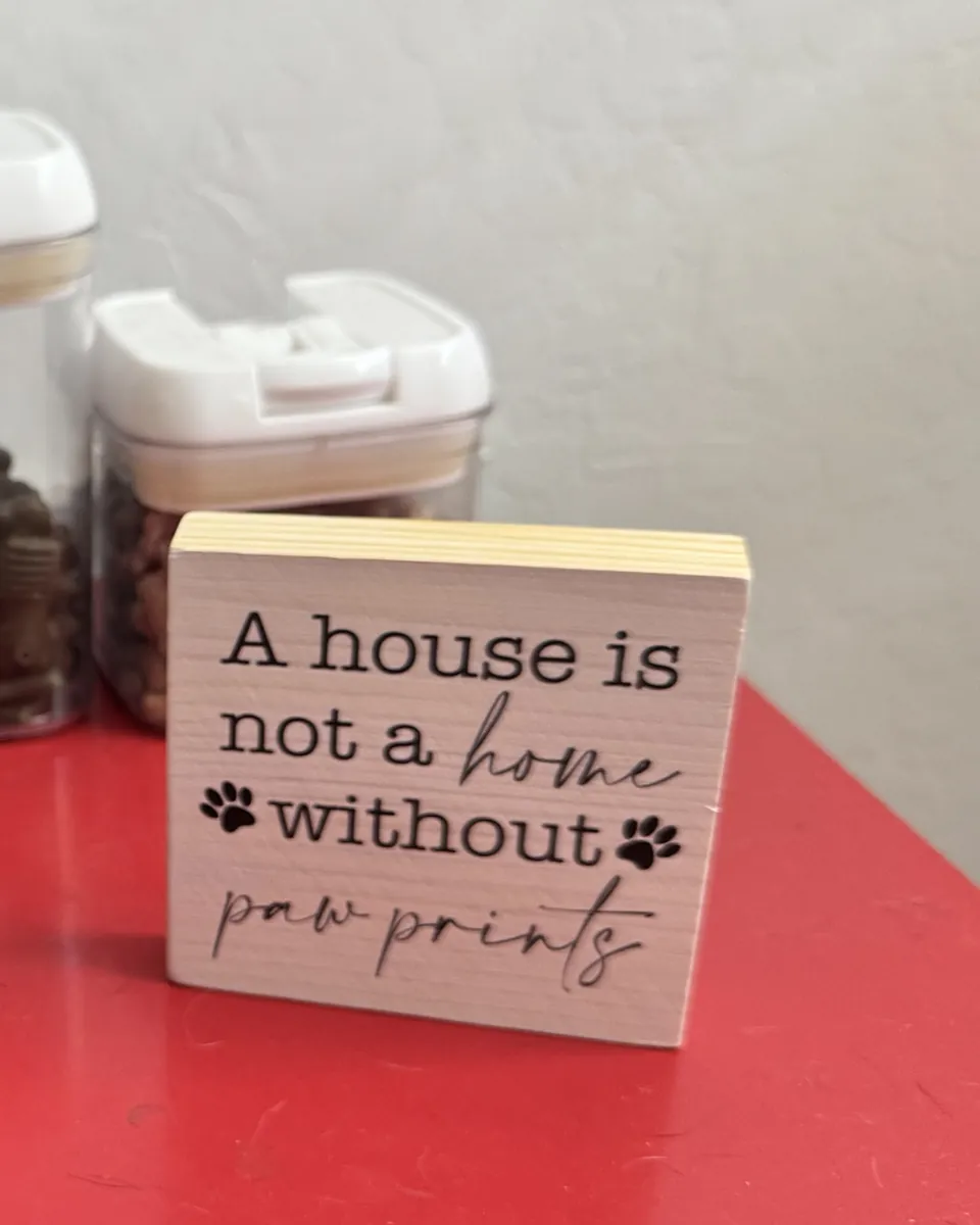 Treat jars beside a small wooden sign that reads “A house is not a home without paw prints”